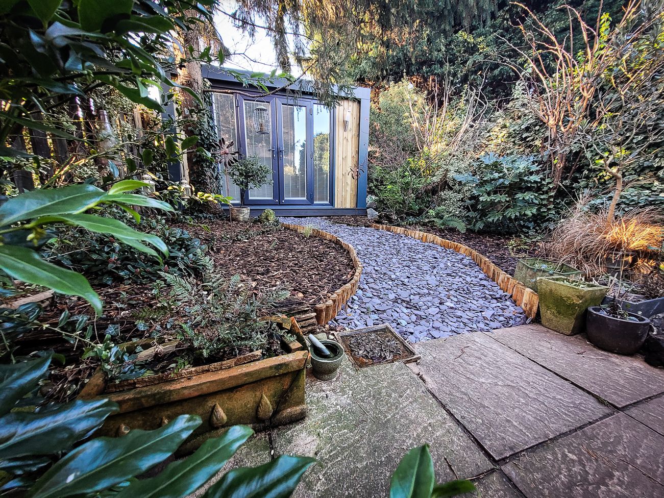 Outside of garden room with greenery either side and curved path leading up from a patio