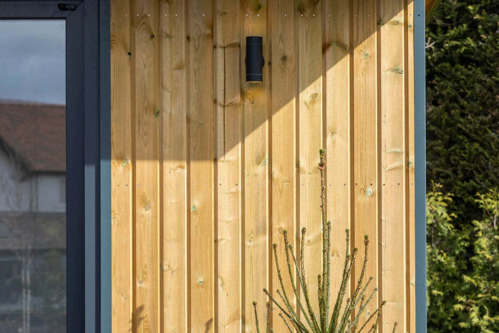 Close-up of redwood garden building cladding with black downlight mounted onto it.