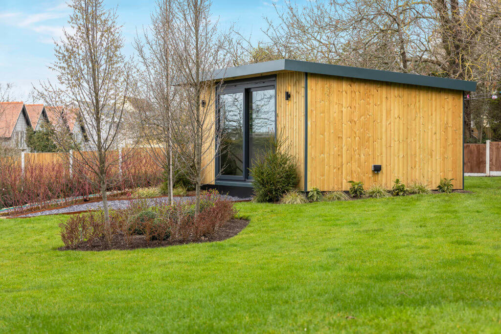Side view of redwood clad garden studio with green lawn in the foreground.