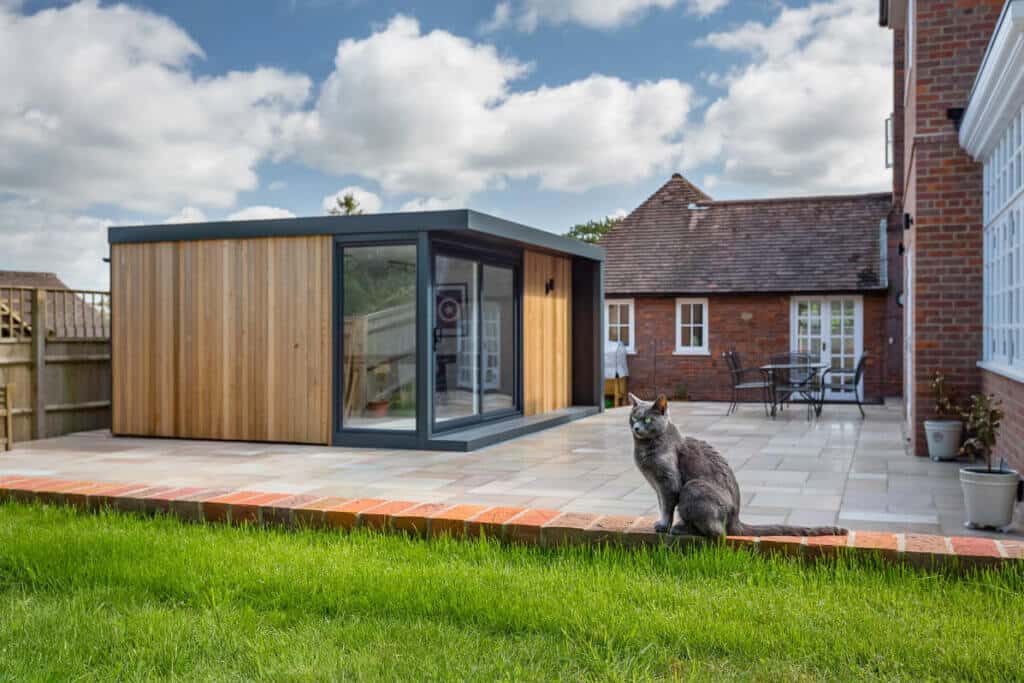 Grey cat sat on brick garden wall in front of wooden garden games room on large patio