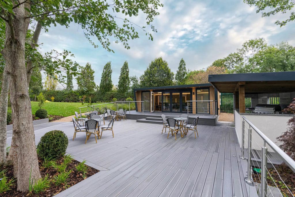 Landscaped garden with a grey patio and bistro furniture with a raised patio and a boardroom on it