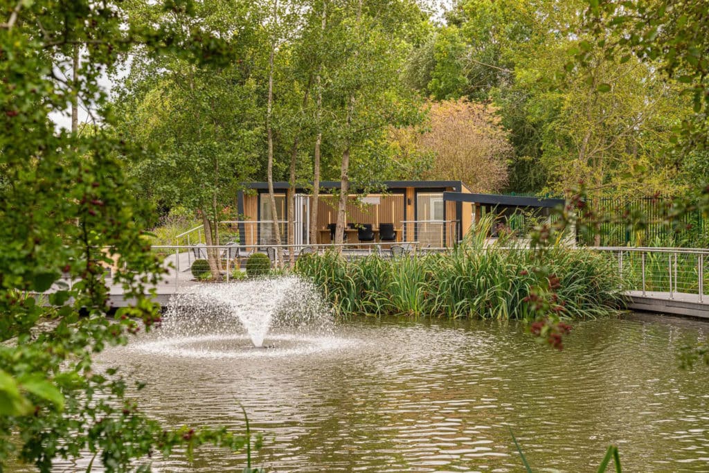 A pond with a water feature and reeds and a meeting room in the background