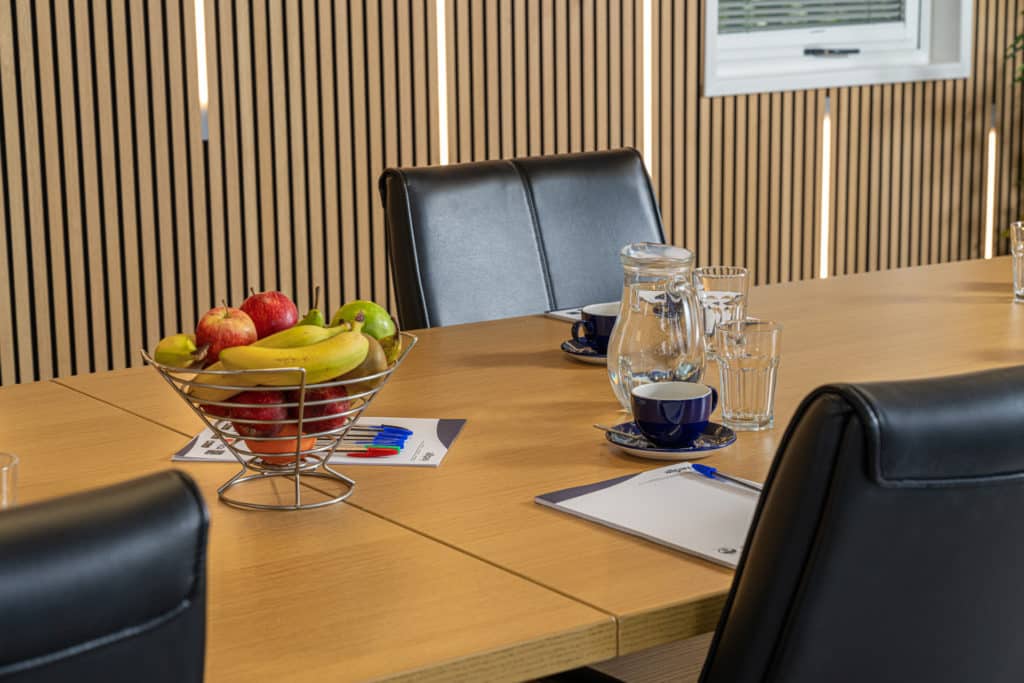 Interior of a boardroom with a close up of a table with fruit, water and cups on it