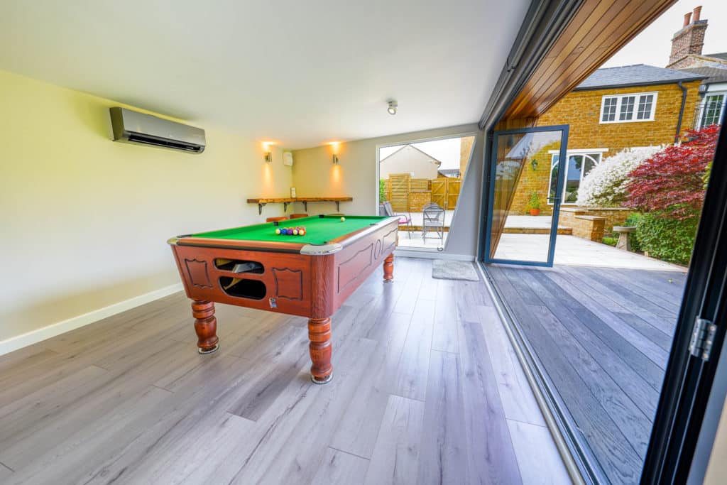 Interior of a man cave with it's bi-fold doors open on the right and a pool table in the centre of the room