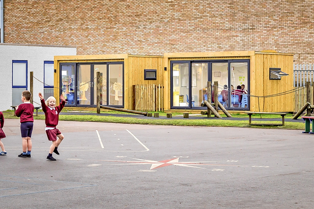Children playing in the playground with two outdoor classrooms from Green Retreats in the background