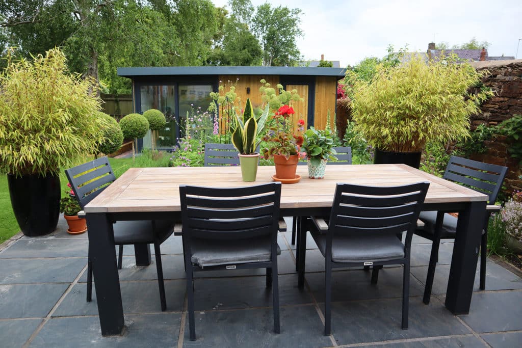Garden room in the back ground with garden table and chairs as main photo feature and tree table plants in the middle