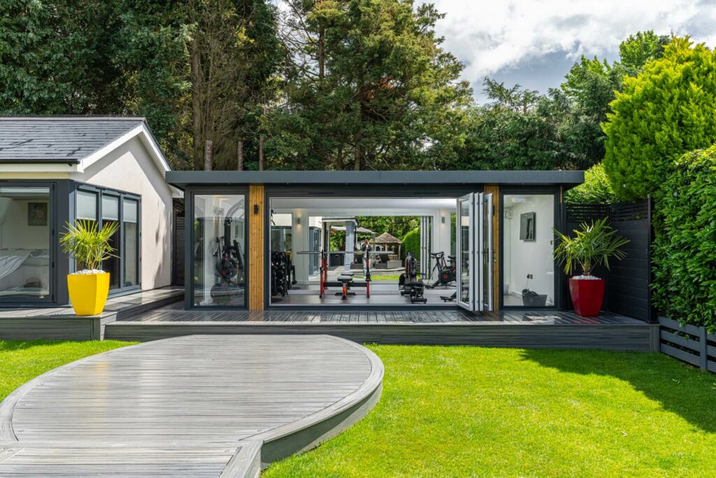 Exterior of modern garden room gym with large bifold doors in manicured garden setting