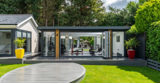 Exterior of modern garden room gym with large bifold doors in manicured garden setting