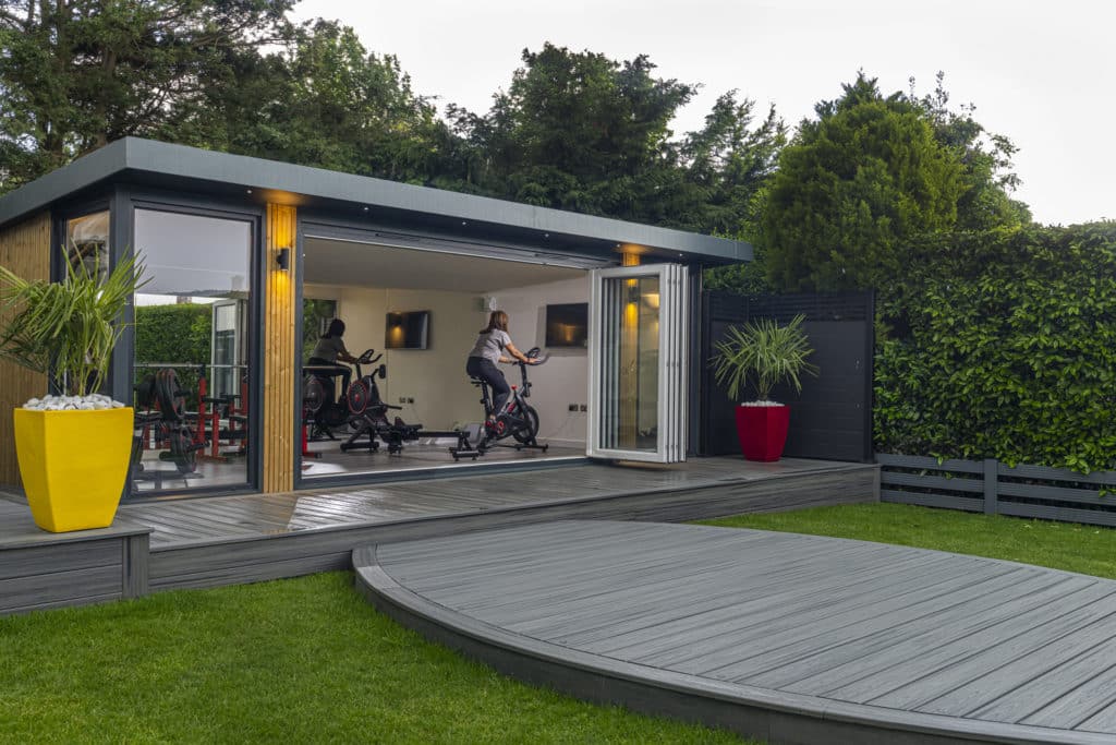Woman riding exercise bike inside garden room gym and dusk