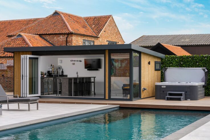A view of a modern garden room with a swimming pool, hot tub & open doors