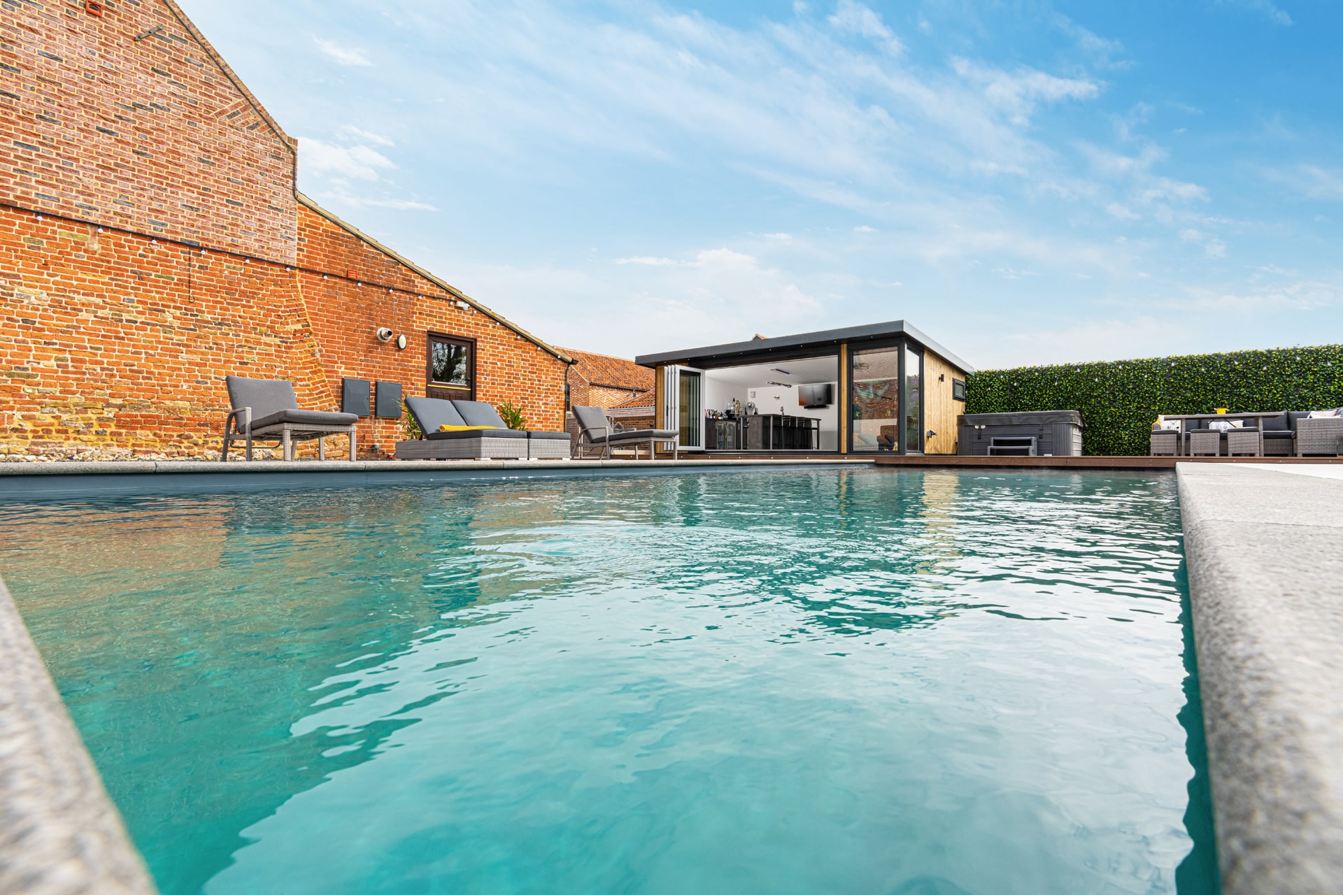 Glistening water in sunken swimming pool with home bar garden room in the background.