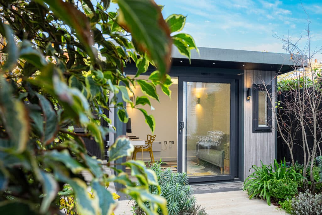 Leaves in the foreground with garden room that is clad in grey composite cladding