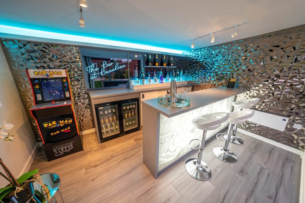Interior of garden bar with light up bar, bar stools, drinks fridge and vintage pac man games machine.