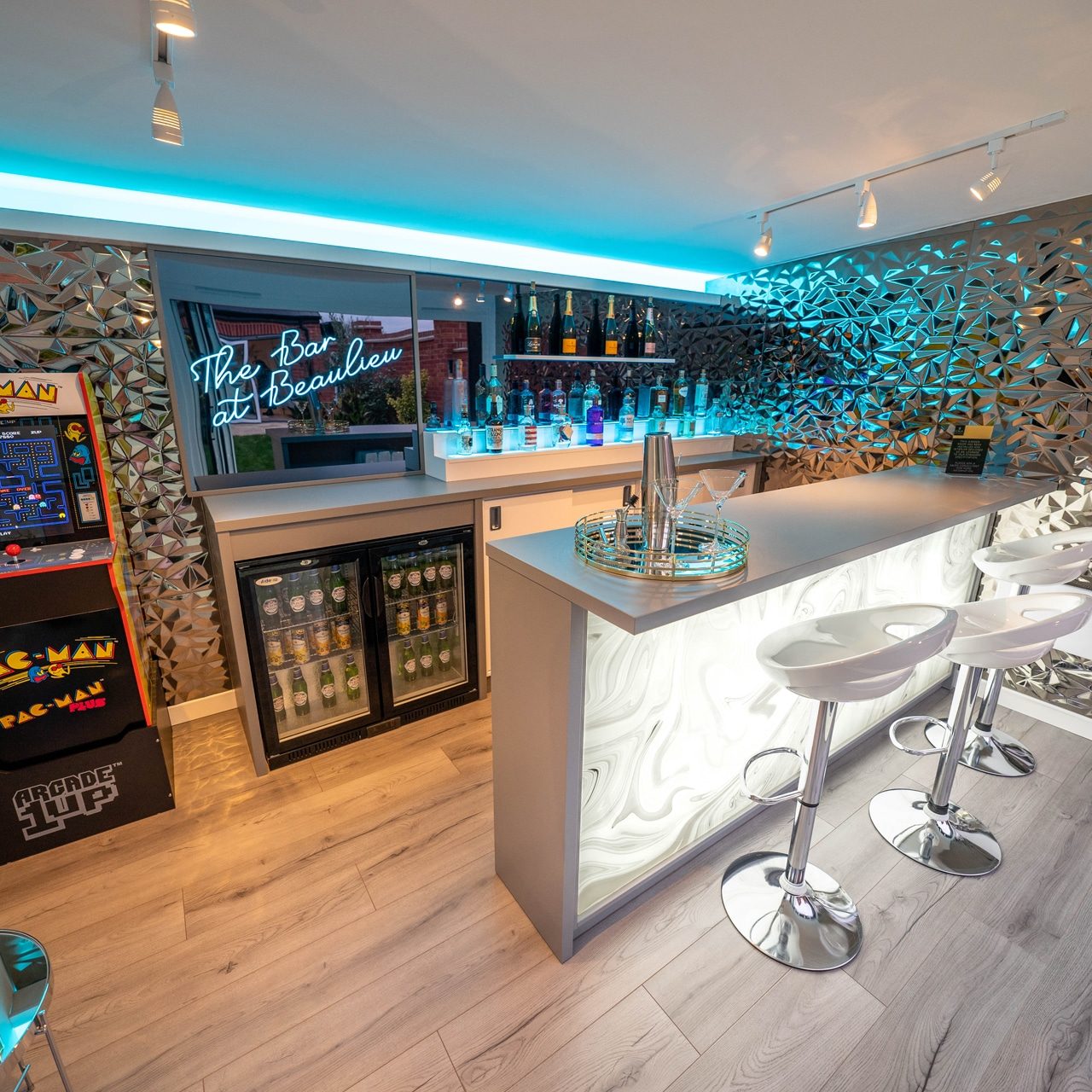 Interior of garden bar with light up bar, bar stools, drinks fridge and vintage pac man games machine.