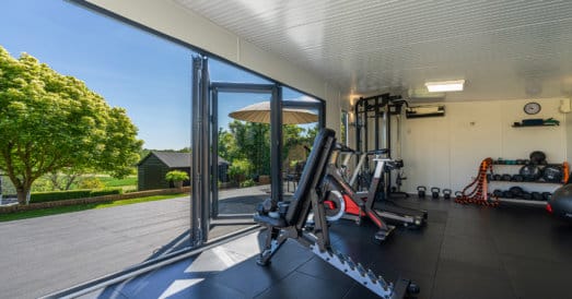 Home gym with bifold doors open on decking and garden beyond a beautiful sunny day.