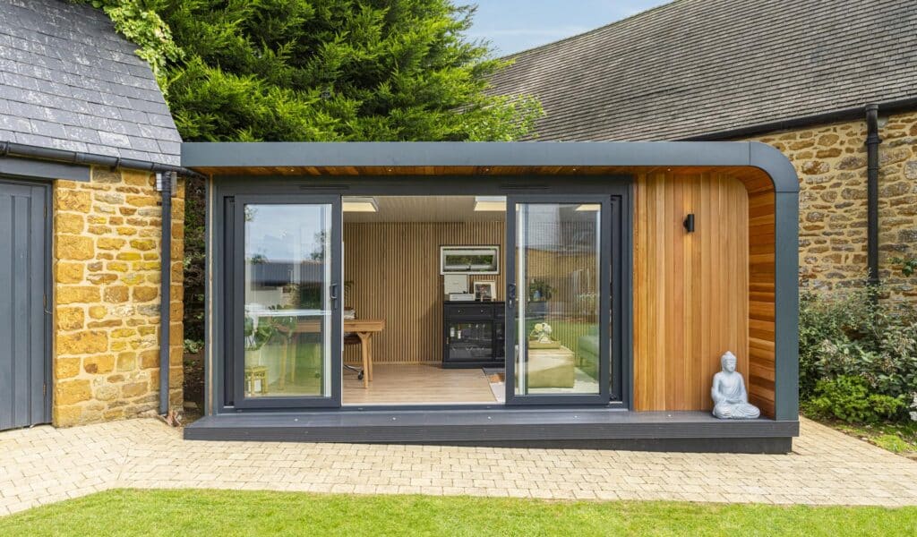 What is a garden room? Front view of cedar clad garden room with sliding doors open to show wooden slatted wall and interior being used as office and lounge