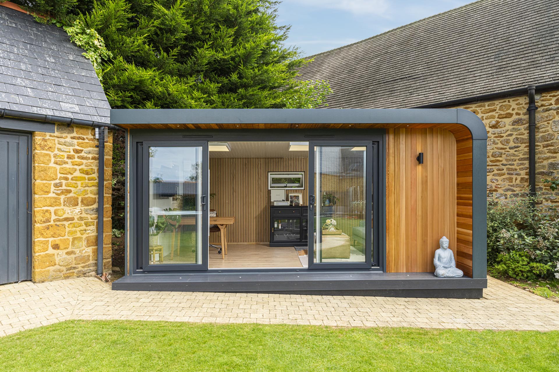 Front view of cedar clad garden room with sliding doors open to show wooden slatted wall and interior being used as office and lounge