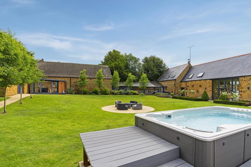 Pano of courtyard garden with hot tub pool in the foreground and view of converted barn house and garden room