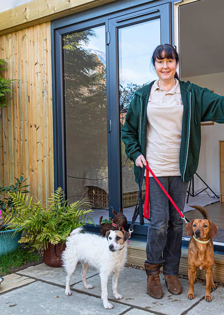 Client with two dogs on a lead standing in front of a garden room