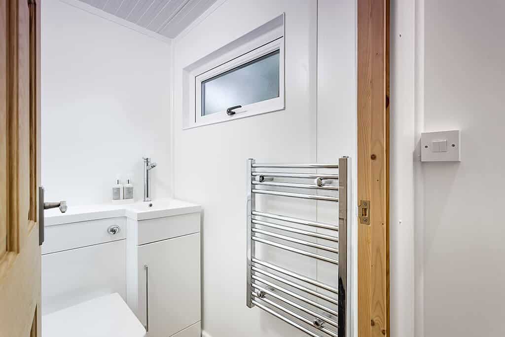 Mounted chrome towel radiator with gloss white bathroom cabinets in the background.