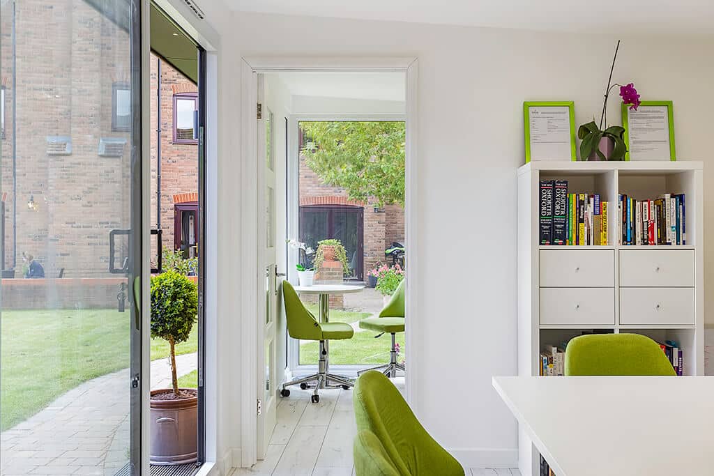 A partition wall in a large garden office provides a smaller meeting room with green office chairs